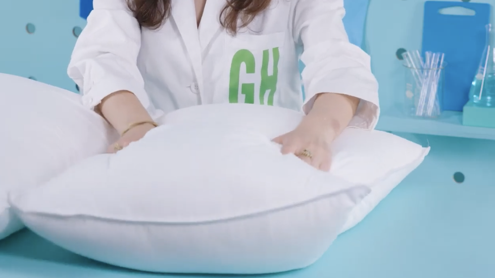 hands pressing down on a down alternative pillow from amazon basics, part of good housekeeping's pillow testing