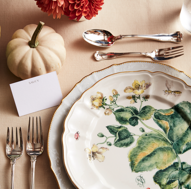 a table setting with a plate with green leaf designs on it surrounded by mini pumpkins