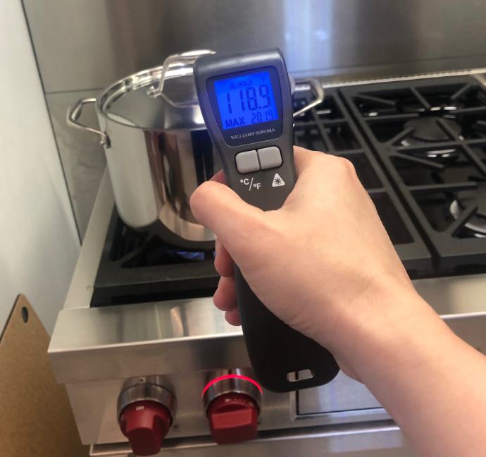 a hand holding an infrared thermometer to take the temperature of a stock pot
