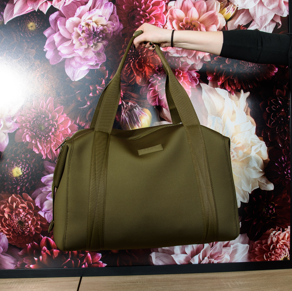 a model holding a green landon carryall bag in front of a floral image, good housekeeping's best weekender bags