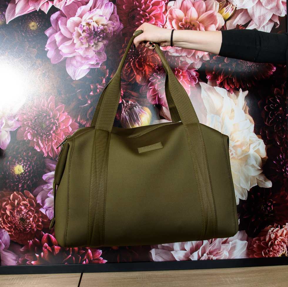 a model holding a green landon carryall bag in front of a floral image, good housekeeping's best weekender bags