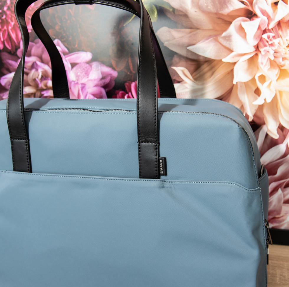 a blue away everywhere large bag in front of a floral backdrop, good housekeeping's best weekender bags