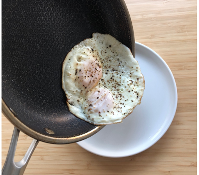 two fried eggs sliding out of a hexclad skillet onto a plate