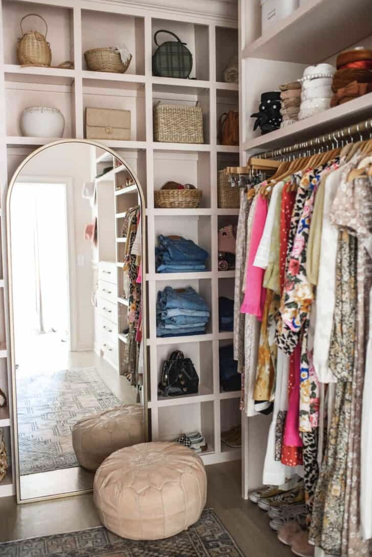a closet with clothes and an ottoman and arched mirror