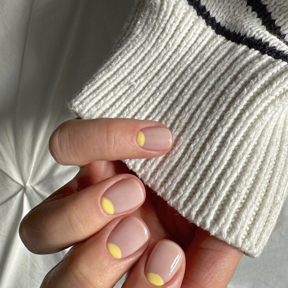 a mão de uma pessoa com unhas pintadas com meias luas amarelas