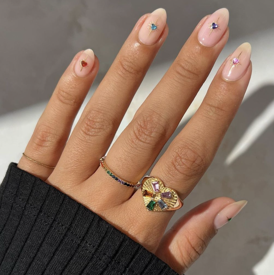 a hand with a ring on it and jeweled manicure