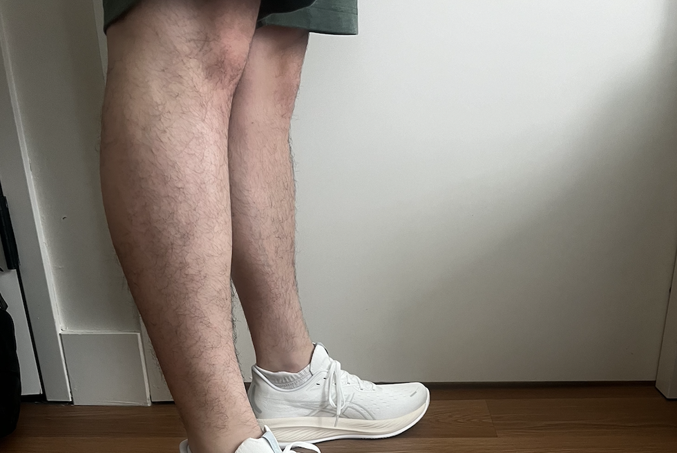 a tester wearing a pair of white asics gel cumulus 26 sneakers on a wooden floor as part of good housekeeping's best walking shoes