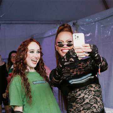 two individuals taking a selfie at an event with a backdrop of a tent two individuals taking a selfie at an event with a backdrop of a tent