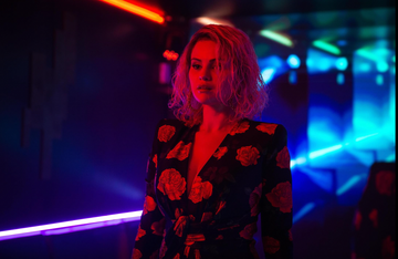 a person wearing a floral dress in a dimly lit environment with neon lights