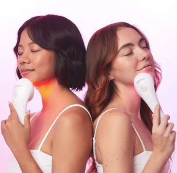 two women holding a device for facial treatment positioned back to back