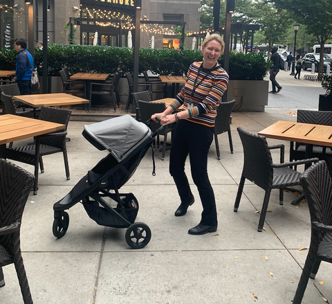 a woman tests a lightweight thule spring stroller outside of a restaurant, part of good housekeeping's tests for best lightweight strollers