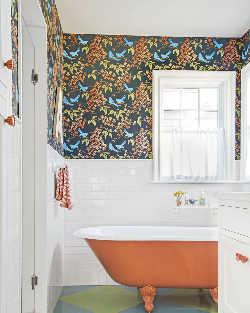 bathroom with white tile half way up the wall and colorful blue and orange wallpaper on a black background a cast iron tub has been painted orange and the wooden floors have been painted in green and blue diamonds that match the tones of the wallpaper