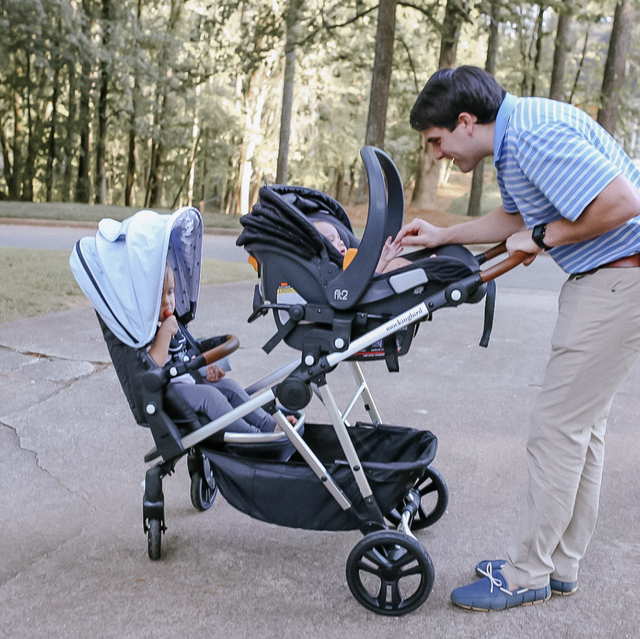 a man tends to his baby in a car seat while his older child sits in a stroller seat, part of a good housekeeping review of the mockingbird single to double stroller and original single stroller