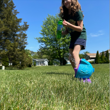 testing for the best bubble machines for good housekeeping magazine a girl tests a bubble machine in a backyard, part of the good housekeeping story on the best bubble machines