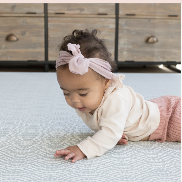 a baby with a white shirt crawls on a blue play mat, part of a good housekeeping list of best baby play mats