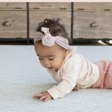 a baby in a white shirt crawls on a blue play mat on the floor