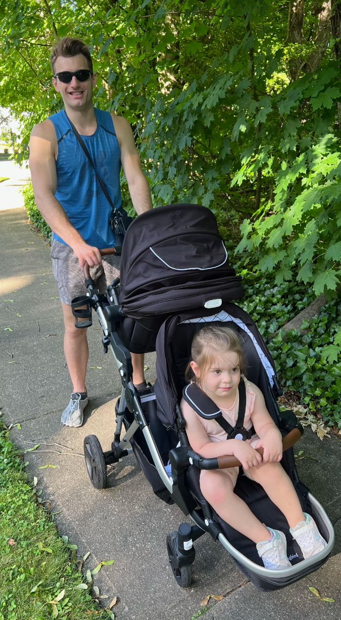 a father pushes a black mockingbird stroller with a toddler in the front and a newborn riding in an infant car seat in back, part of good housekeeping's tests for the best baby strollers