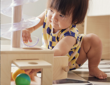 a toddler plays with a ball run that ends at a wooden box, a developmental learning toy from lovevery, part of a good housekeeping story on baby subscription boxes