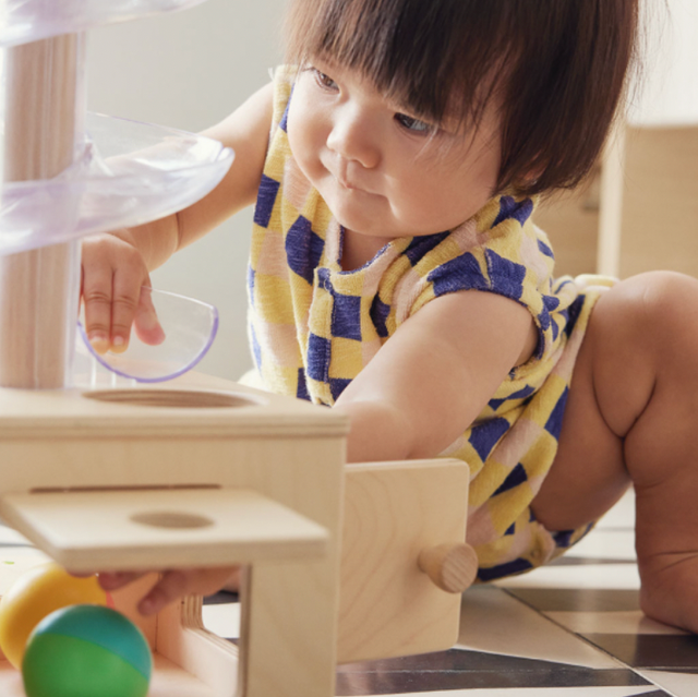 a child plays with a developmental toy from a baby toy subscription box a toddler plays with a ball run that ends at a wooden box, a developmental learning toy from lovevery, part of a good housekeeping story on baby subscription boxes