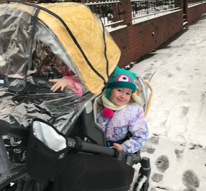 a baby in a double stroller on a snowy sidewalk