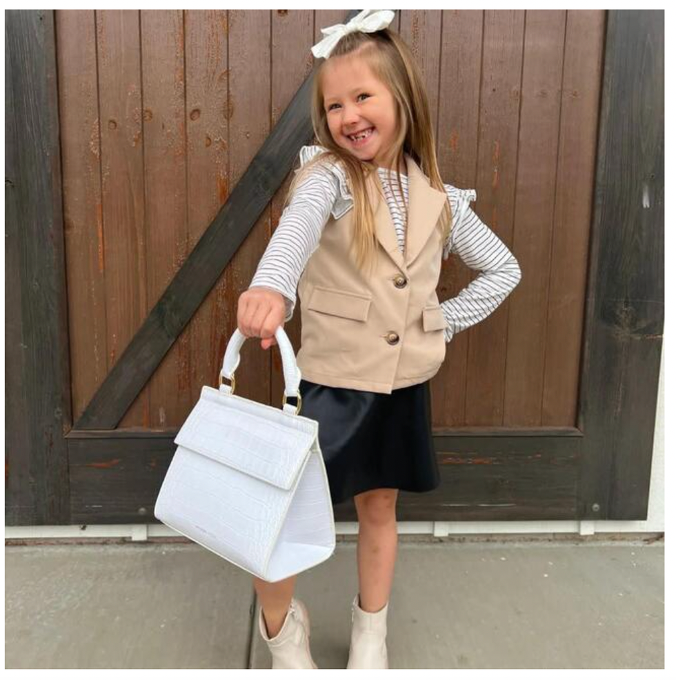 a girl in a beige vest holds a white tote that is actually a lunch box from modern picnic, part of a good housekeeping list of the best kids lunch boxes