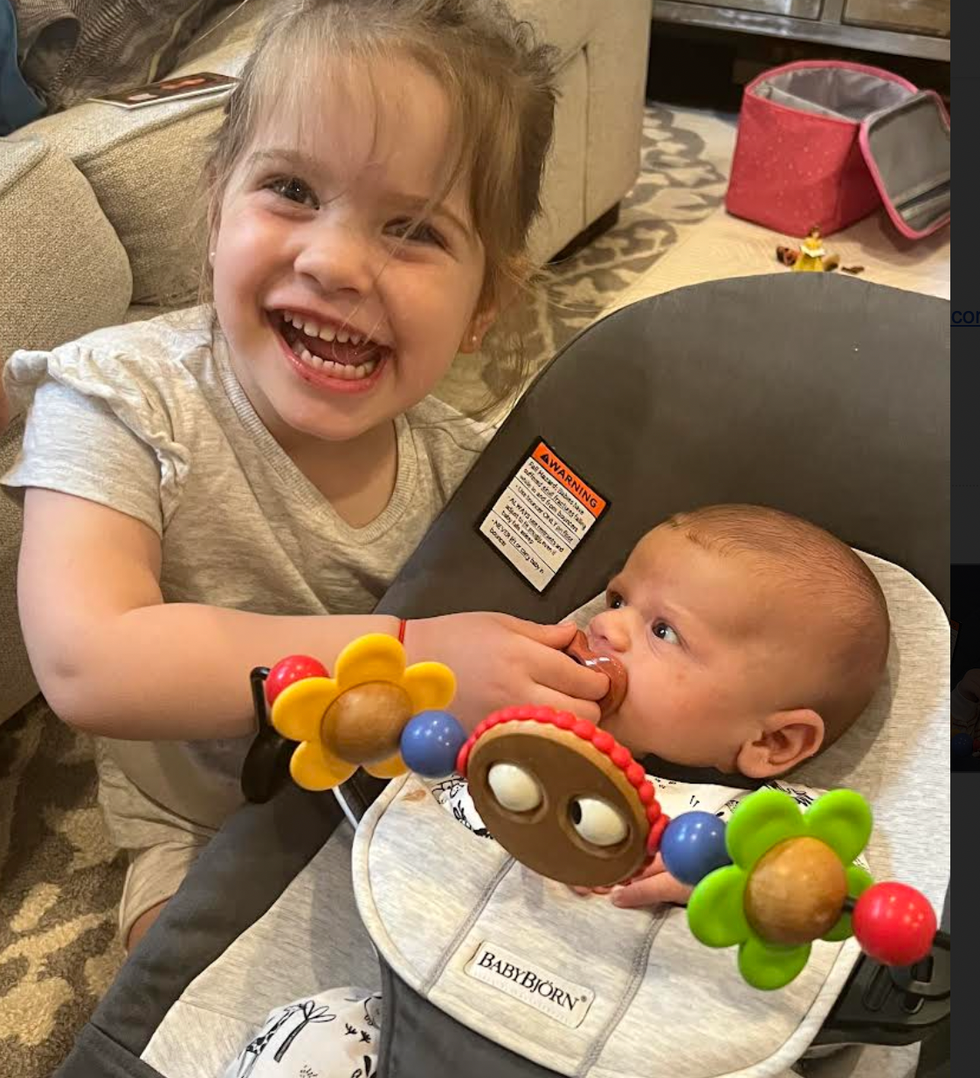 a big sister holds a pacifier in her baby brother's mouth