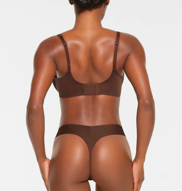 the back of a woman modeling a brown bra from skims against a grey background