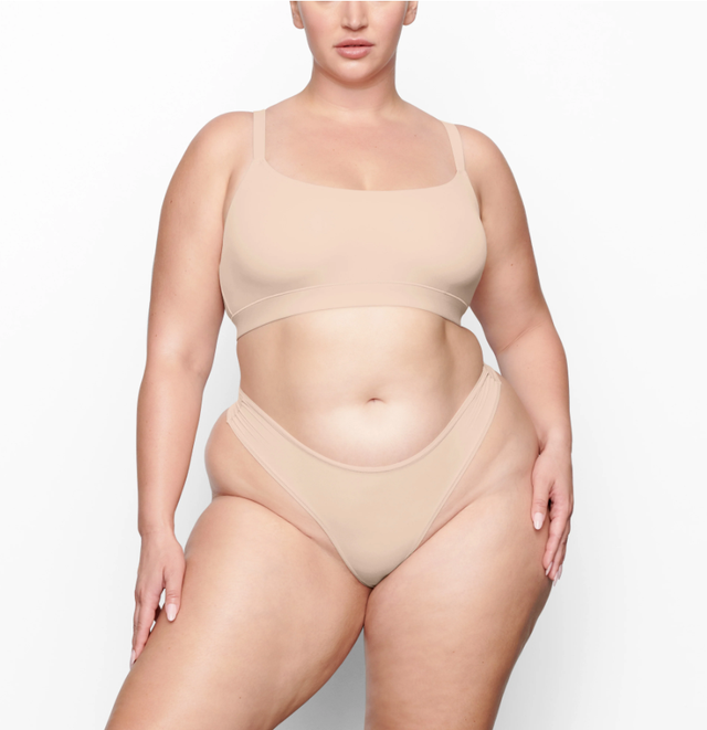 a woman modeling a light tan bralette from skims
