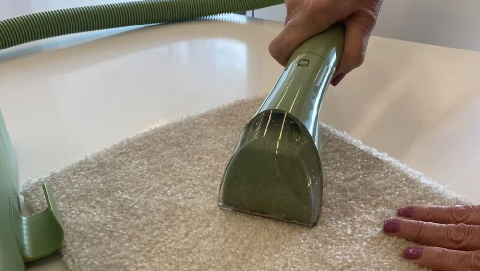Best Carpet Cleaners for Pets: Bissell Little Green Machine in the GH Cleaning Lab woman's hands using the bissell little green machine in the gh cleaning lab on a carpet swatch in the cleaning lab