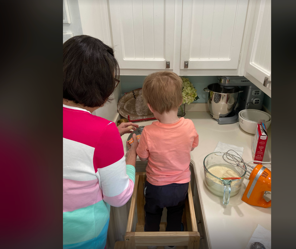 a grown up in a striped sweater guides a child through baking while they child stands on a learning tower, part of a good housekeeping story on the best learning towers