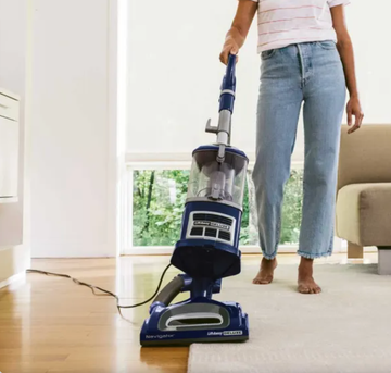 a woman in jeans vacuuming a white rug and hardwood floors