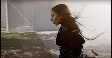 person in a black outfit walking outdoors with long hair flowing in the wind