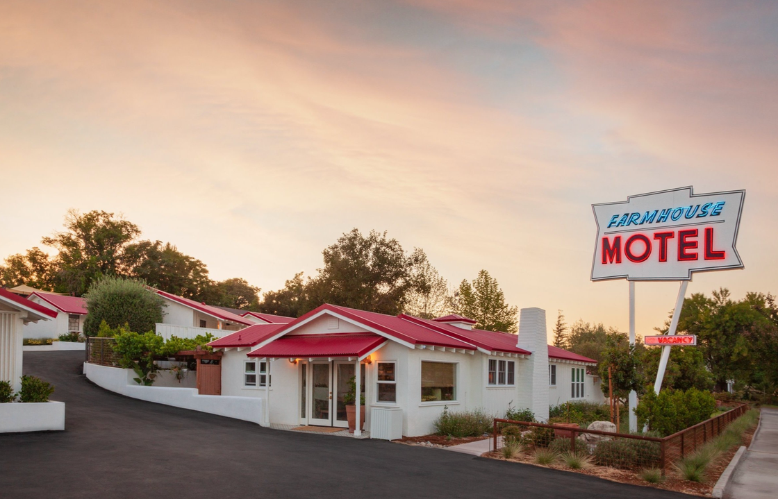 white motel exterior with red roof and a neon sign