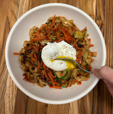 bowl of stir fried noodles and vegetables topped with a poached egg