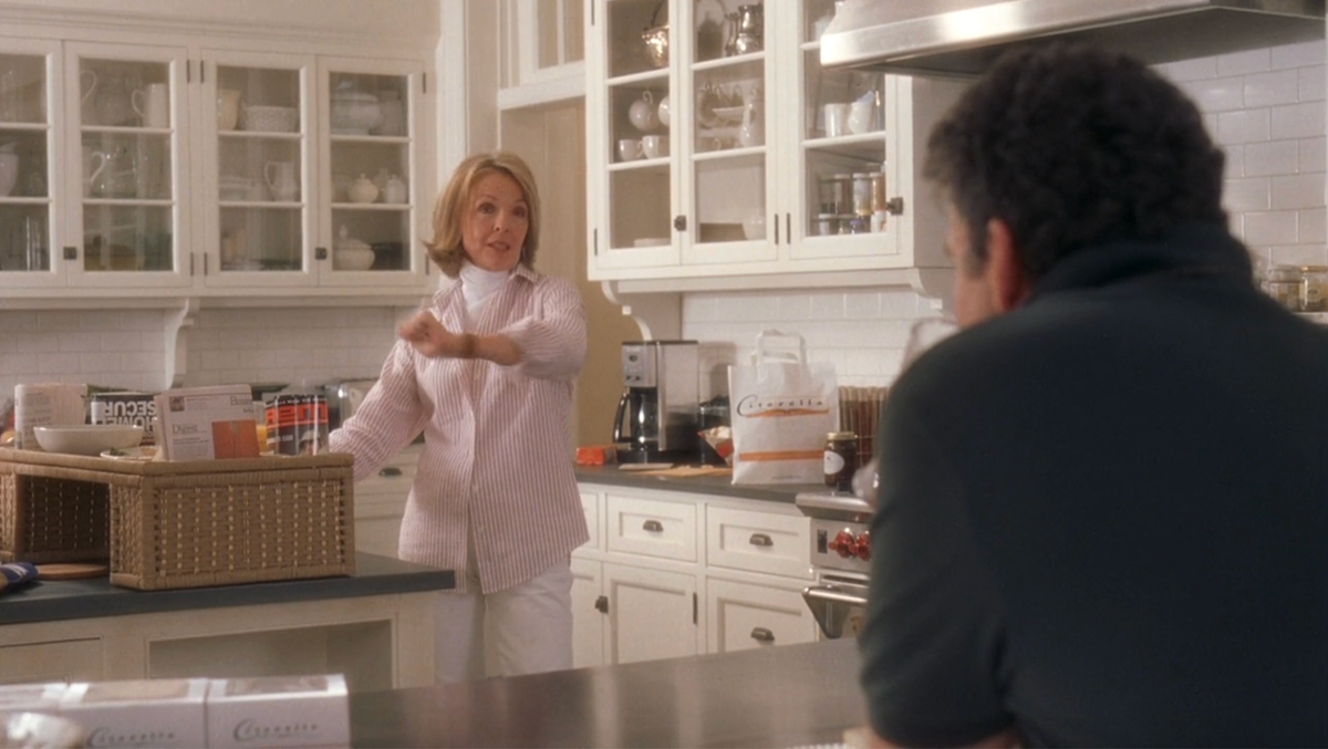 a kitchen scene with a person gesturing towards another individual while standing by a countertop