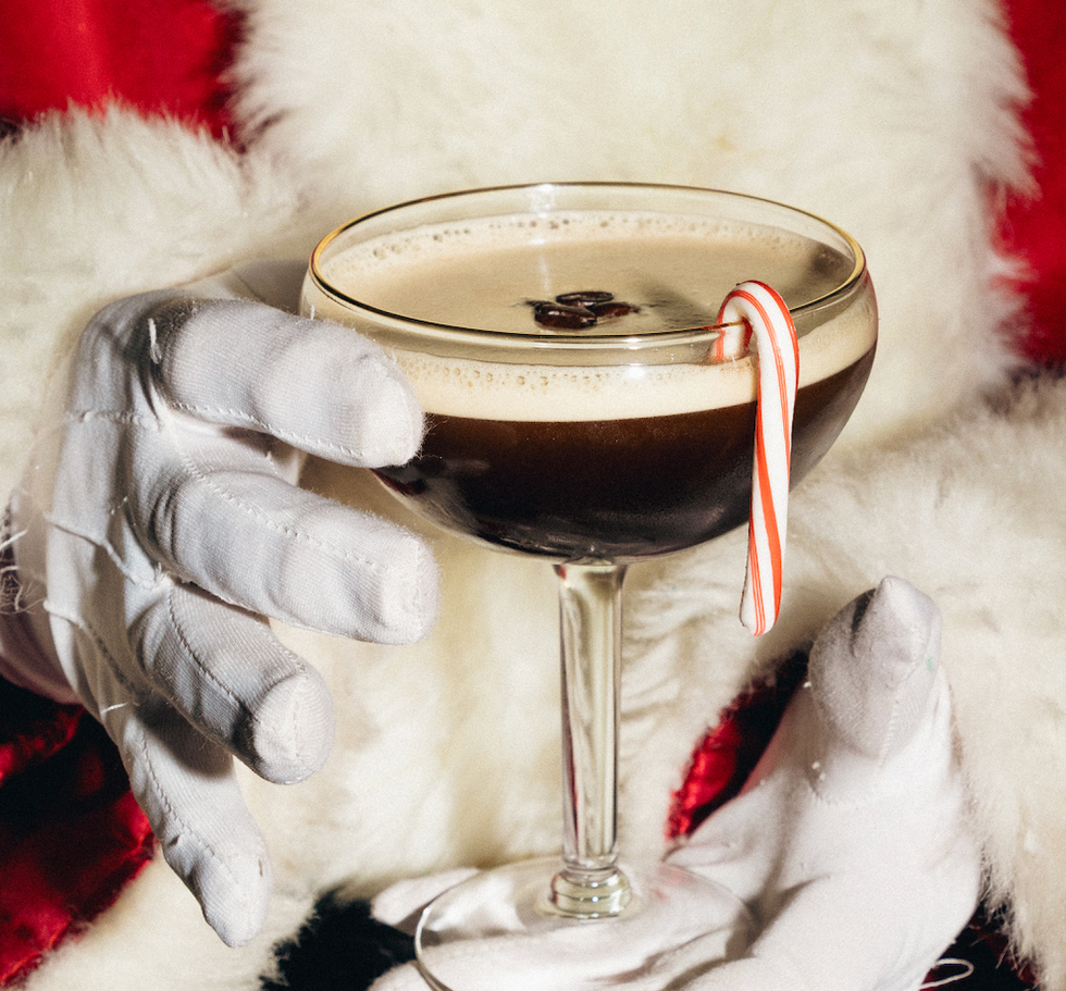 a cocktail with a candy cane garnish held by a gloved hand