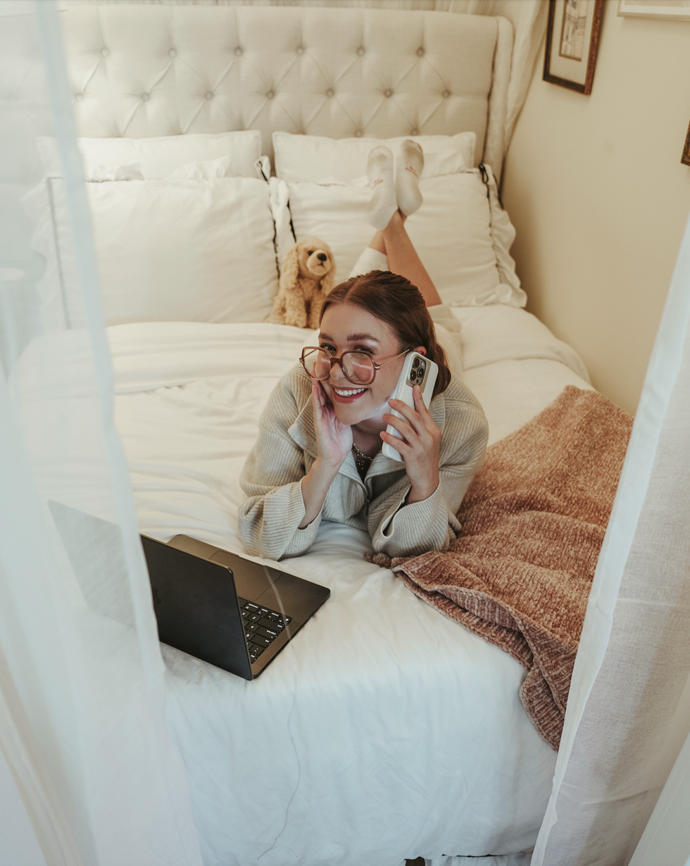 person lying on a bed using a phone and a laptop