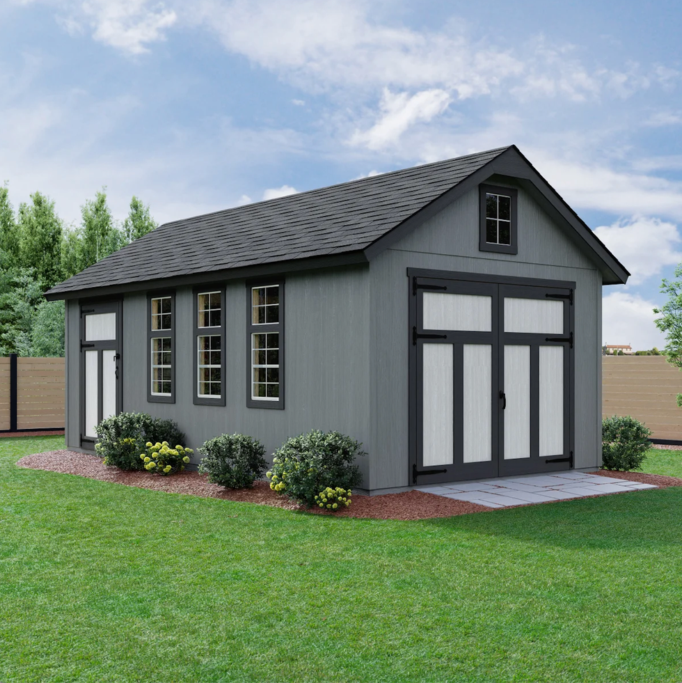 exterior view of a gray shed with multiple windows and a double door surrounded by greenery