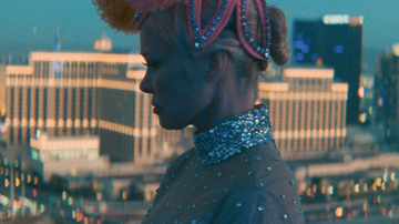 profile view of a woman wearing a jeweled outfit and ornate headpiece against a city skyline