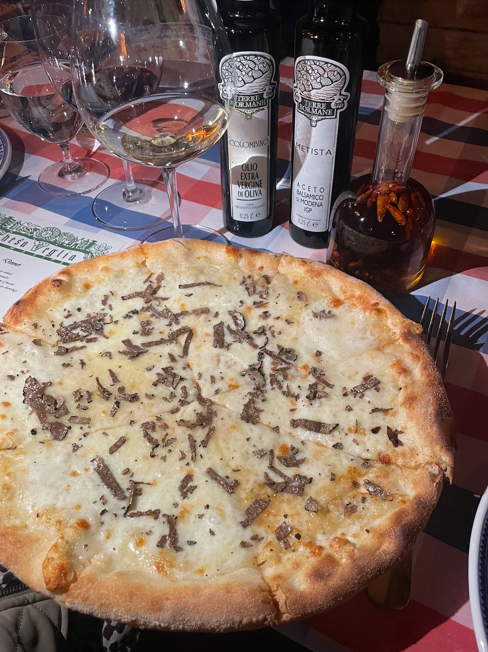 a gourmet pizza topped with cheese and truffle shavings accompanied by olive oil and balsamic vinegar