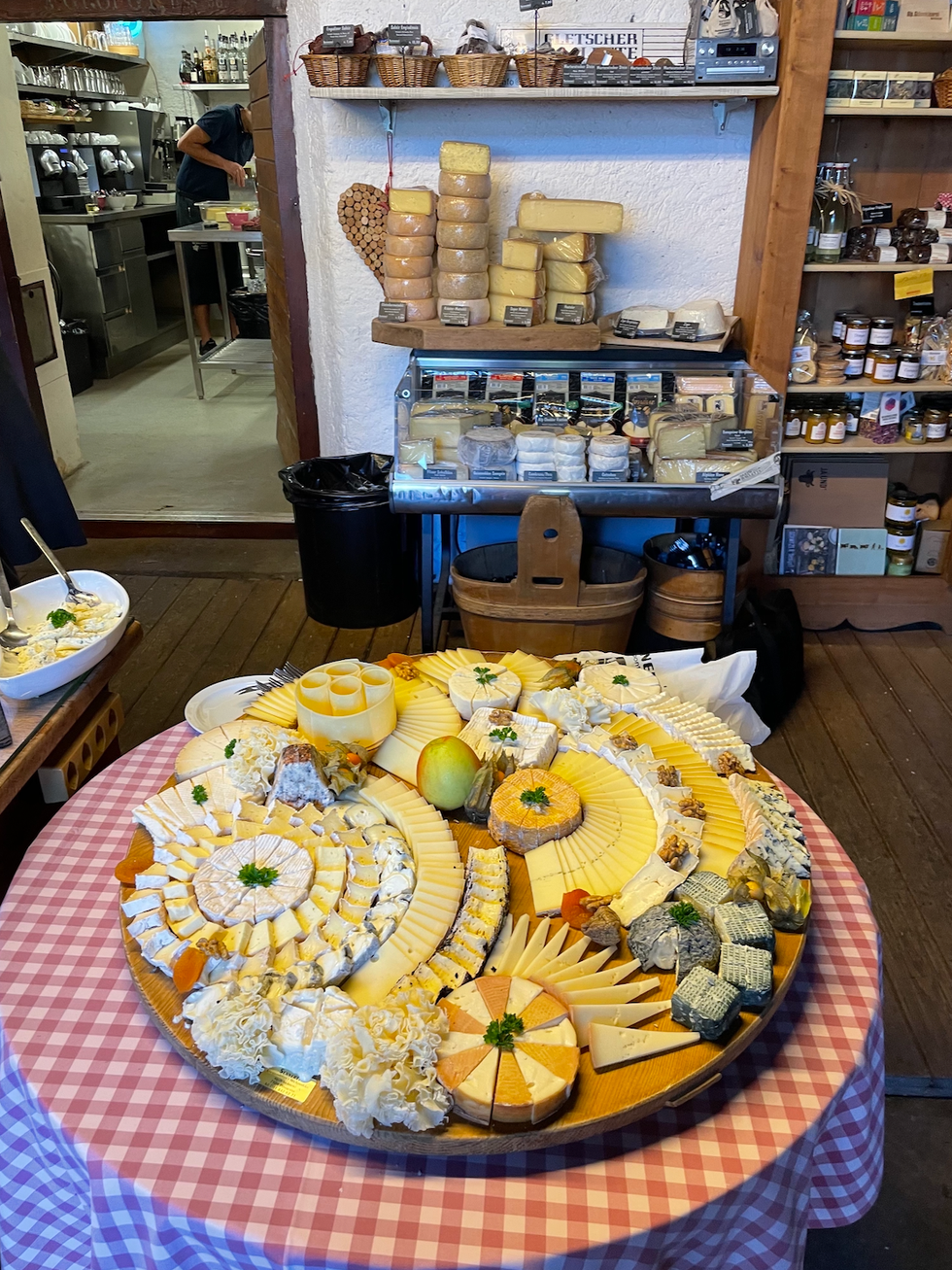 a large selection of various cheeses arranged on a wooden platter displayed in a market or store setting