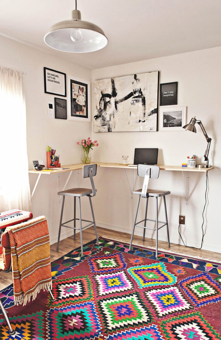 a modern workspace featuring a wooden desk with two bar stools decorative wall art and a colorful patterned rug