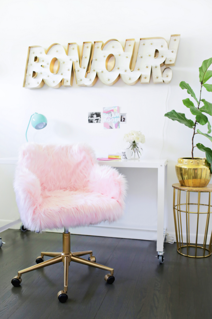 a cozy workspace featuring a pink fluffy chair and decorative elements