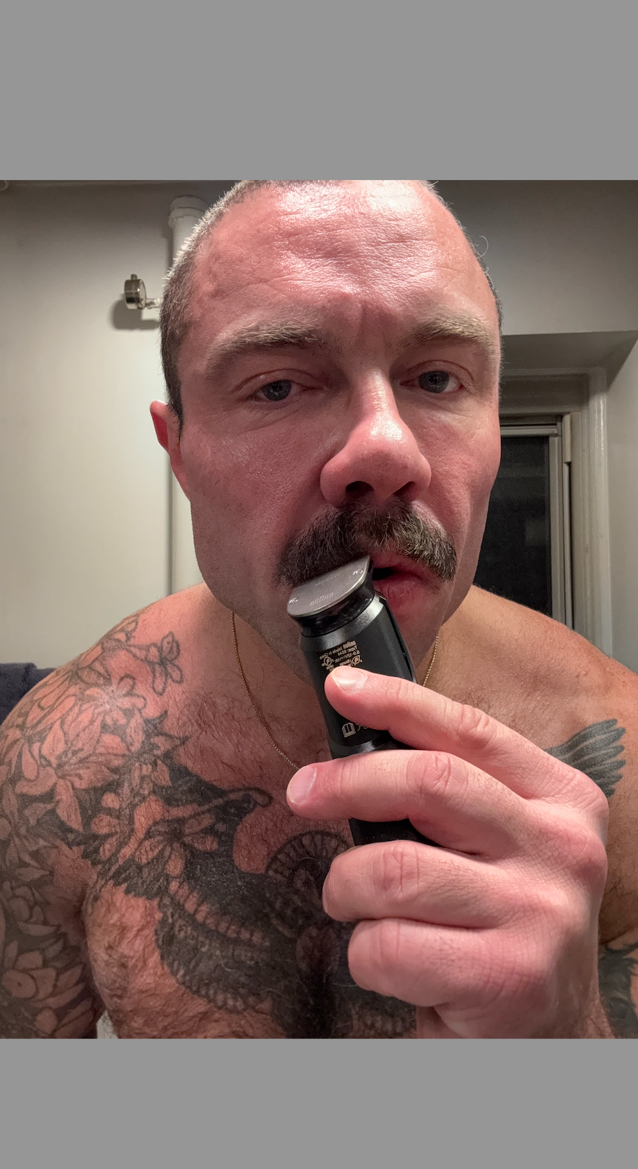 a closeup of a tattooed chest and arm conserving a grooming gadget