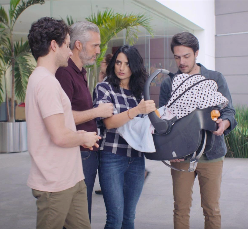 a group of four individuals interacting while holding a baby carrier