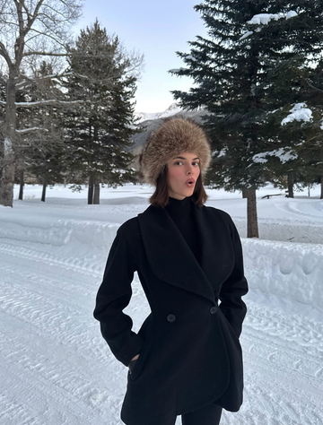 person wearing a winter coat and fur hat standing in a snowy landscape