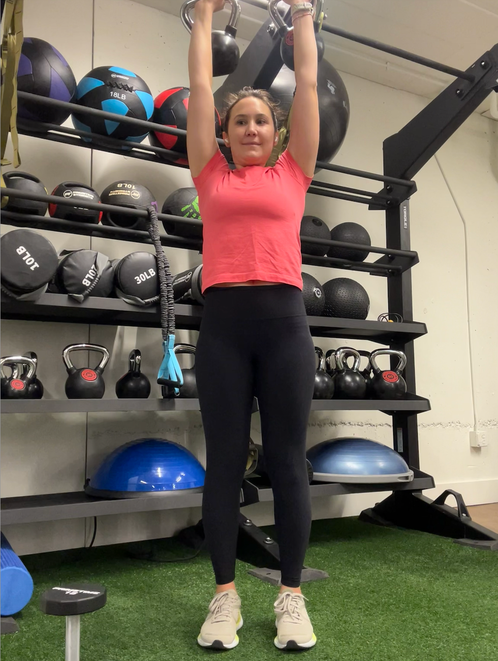 person performing an overhead exercise with kettlebells in a gym