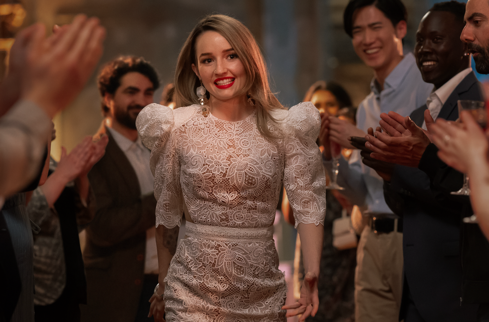 a woman wearing a lace dress is walking through a crowd of applauding guests at an event