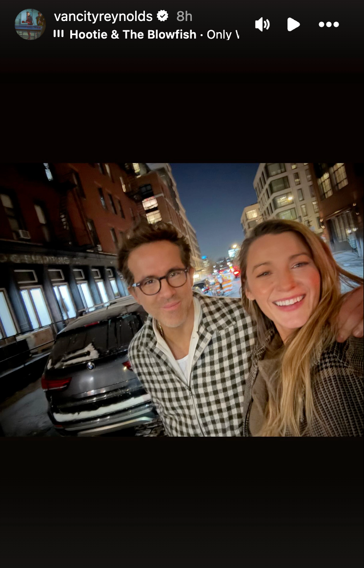 two individuals posing on a city street at night with a parked car and urban buildings in the background