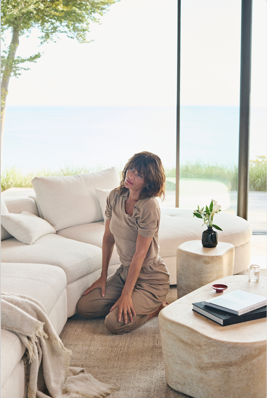 a person kneeling on a rug in a modern living space with large windows and a view of the ocean